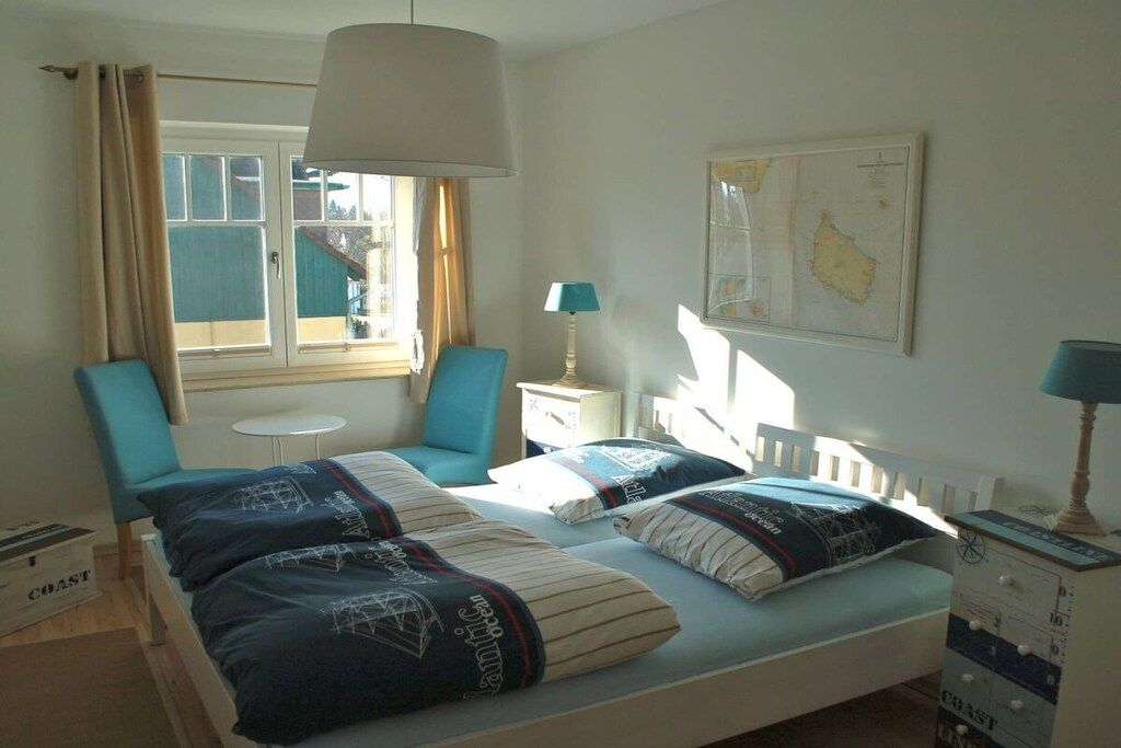 Et soveværelse med to senge, et vindue med gardiner, et kort på væggen og et lille bord.