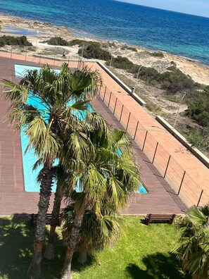 A pool area with a wooden deck, palm trees, and a view of the beach and ocean. - Apartment 'Sea Breeze I La Manga' with Sea View, Wi-Fi and Air Conditioning (La Manga del Mar Menor)
