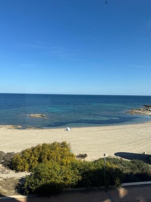 Une plage avec une eau d’un bleu limpide, une tente et quelques plantes vertes au premier plan.