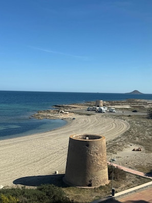 Eine Küstenlandschaft mit Sandstrand, einem großen Betonbauwerk und einem fernen Berg.
