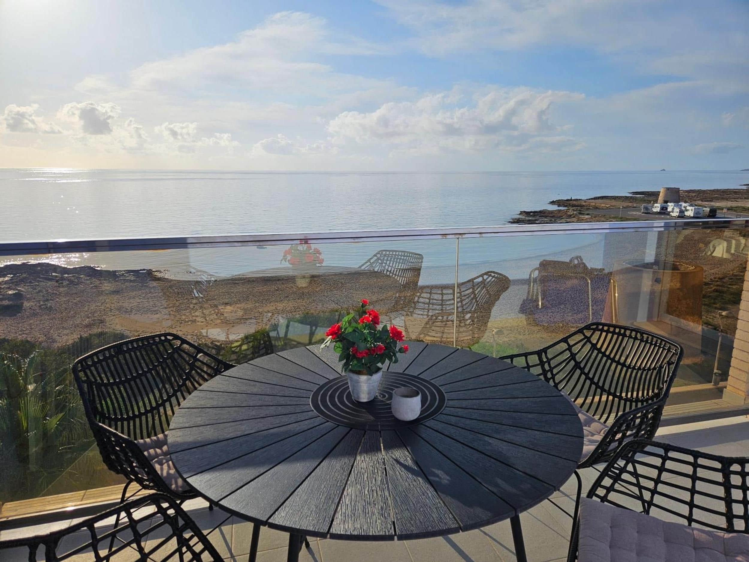 A round table with chairs on a balcony overlooking a body of water and a distant island.