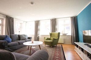 A living room with a sofa, armchair, and TV stand. - Holiday apartment in Barth with swimming pool (Barth)
