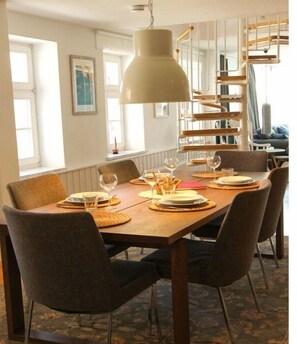 A dining area with a wooden table set for four, surrounded by chairs, with a pendant light above. - Holiday apartment in Barth with swimming pool (Barth)
