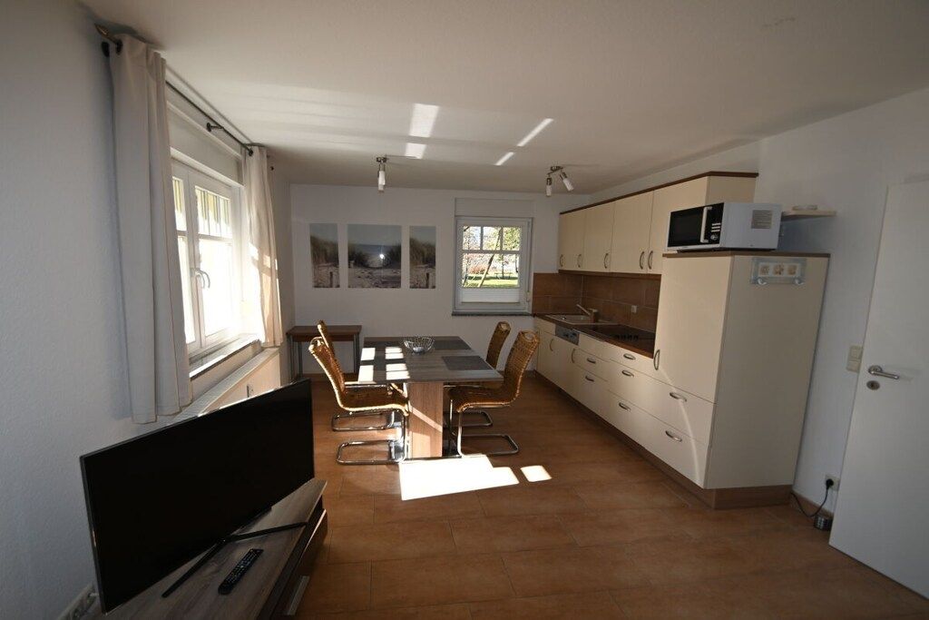 A compact kitchen with a dining area, a flat-screen TV, and a window with curtains.