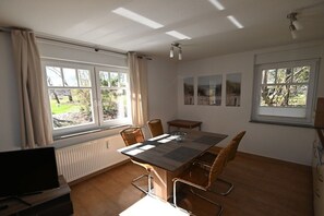 A room with a dining table, chairs, a TV, and windows with curtains. - Holiday apartment with 1 bedroom (Prerow)