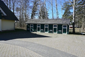 A building with a tiled roof and multiple windows, surrounded by a paved area and trees. - Holiday apartment with 1 bedroom (Prerow)