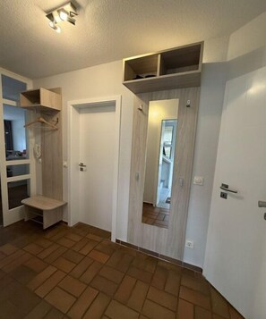 A hallway with a wooden bench, a door with a mirror, and a shelf with hanging items. - Holiday apartment with 1 bedroom (Ostseebad Prerow)