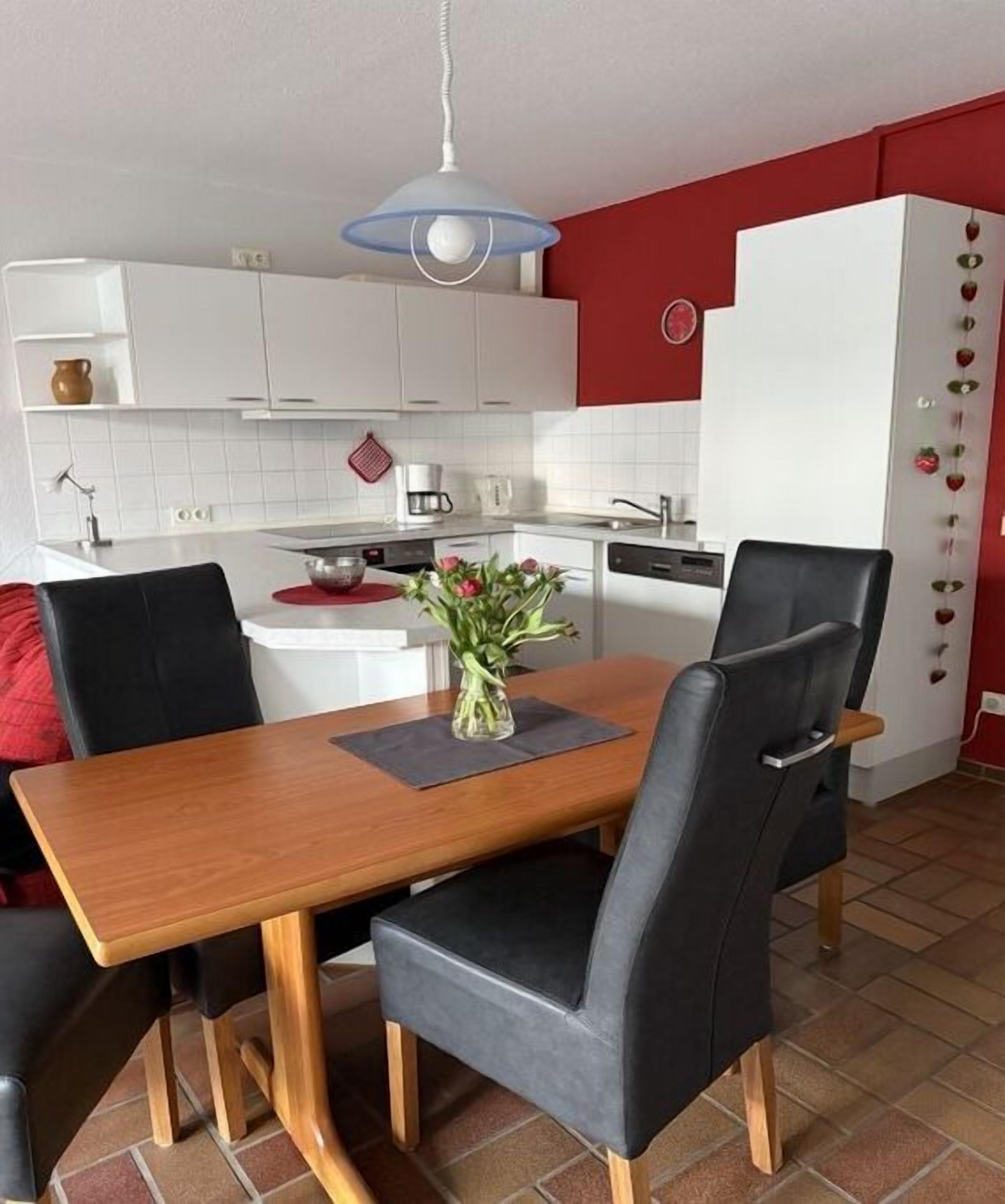 A modern kitchen with white cabinets, a dining table with chairs, and a hanging light fixture.