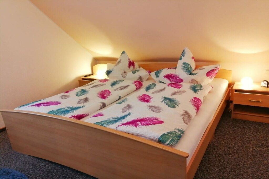 A bed with a floral bedspread and pillows, a wooden headboard, a bedside table with a lamp, and a nightstand with a clock.