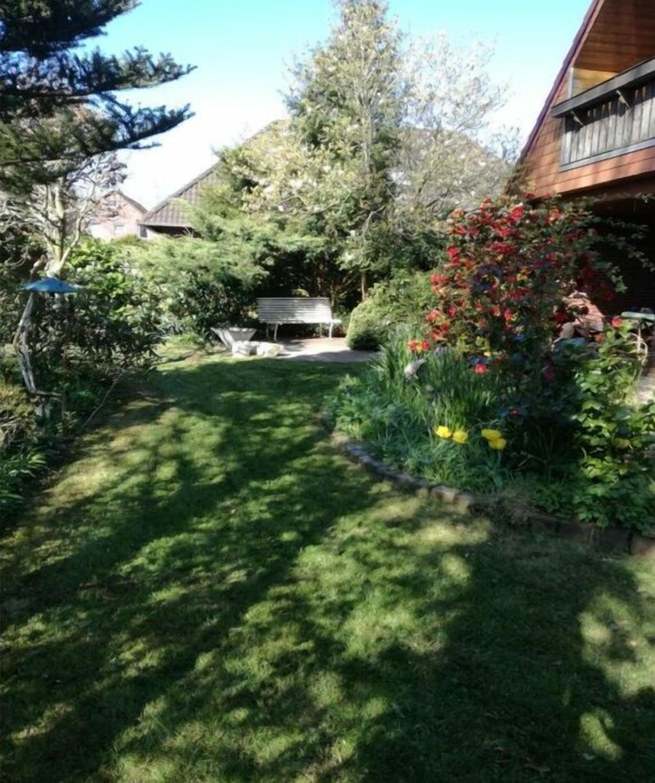 En velholdt have med græsplæne, træbænk og mange forskellige planter og blomster.