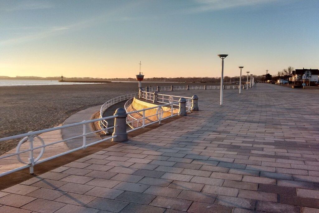 A paved walkway with a railing, a lamp post, and a distant view of a body of water.