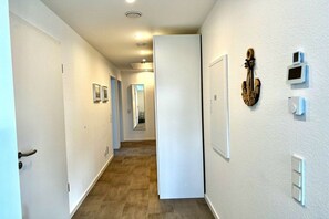 Um corredor com uma porta dando para um quarto, um interruptor de luz fixado na parede e um termostato na parede.