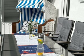 A table with a glass bottle, a glass of water, and a small vase with flowers. There are two chairs with cushions and a striped umbrella. - Holiday apartment in Baabe with swimming pool (Baabe)