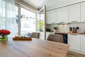 Eine moderne Küche mit weißen Schränken, einem Holztisch und Blick durch große Fenster.