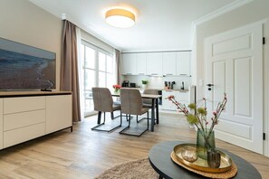 Ein modernes Wohnzimmer mit Fernseher, Essbereich mit Stühlen, Küche mit Schränken und einem großen Fenster.