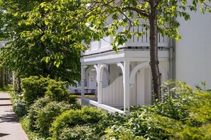 Ein weißes Gebäude mit einer überdachten Veranda und einem Baum im Vordergrund.
