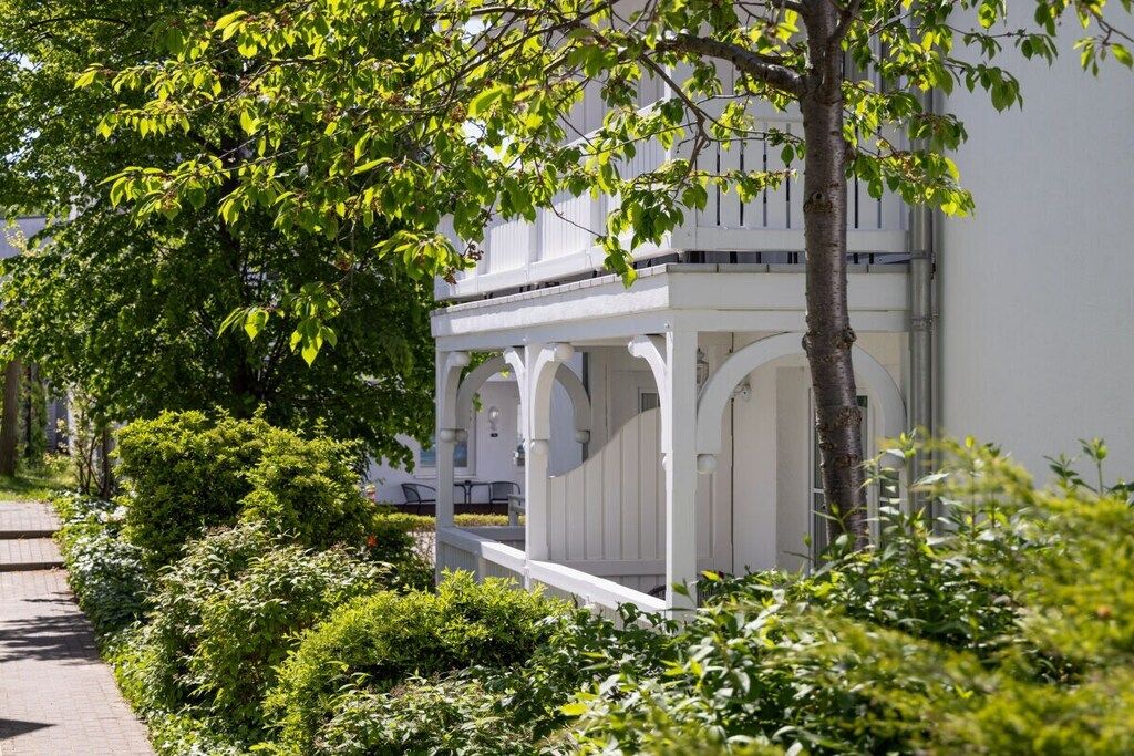 A white building with a covered porch and a tree in the foreground.