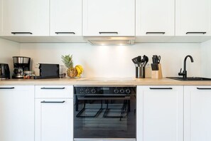 Una cocina moderna con armarios blancos, extractor Bosch, horno integrado y una encimera con cafetera, fruta y utensilios.