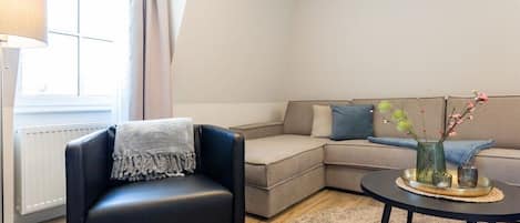Una sala de estar moderna con un sillón de cuero negro, un sofá seccional color beige y una mesa de centro redonda con un jarrón de flores.
