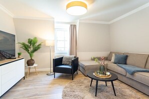 A modern living room with a sofa, armchair, coffee table, and a TV on a cabinet. - 6 (Starfish) in Villa Vesta (Ostseebad Binz)