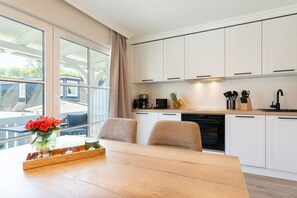 Una cocina moderna con armarios blancos, una mesa de comedor de madera y una ventana con vista a una casa.