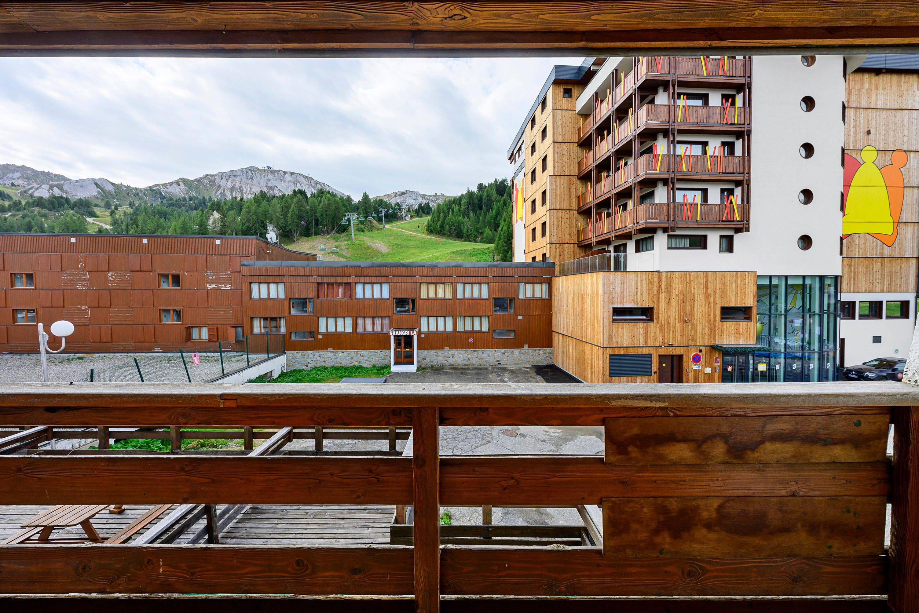 Un edificio de madera con un telesilla de fondo, rodeado de montañas.