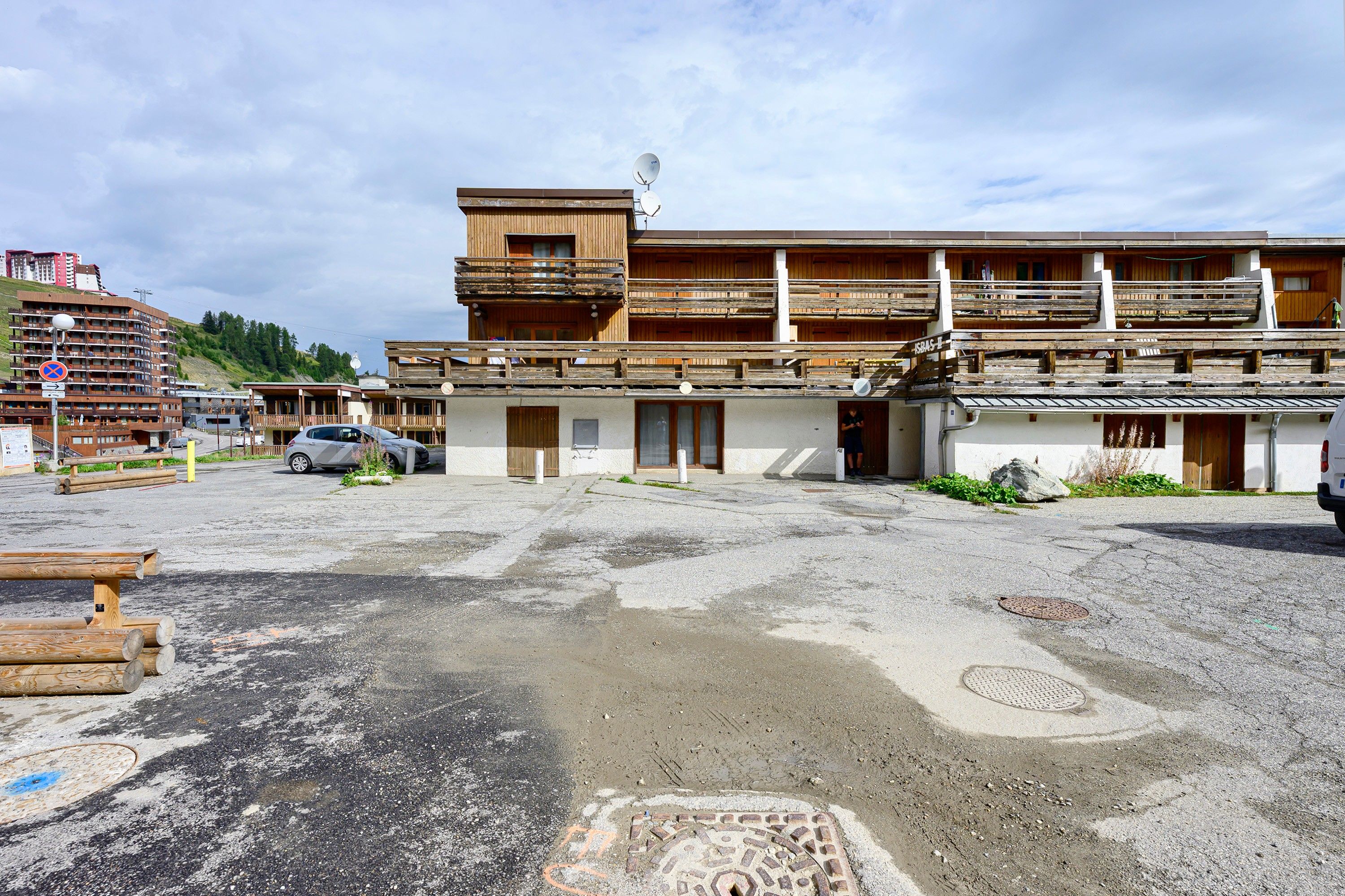A building with a wooden facade, multiple balconies, and a parking area with a car.