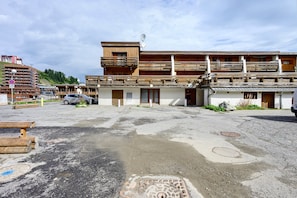 Un edificio con fachada de madera, varios balcones y un estacionamiento con un coche.
