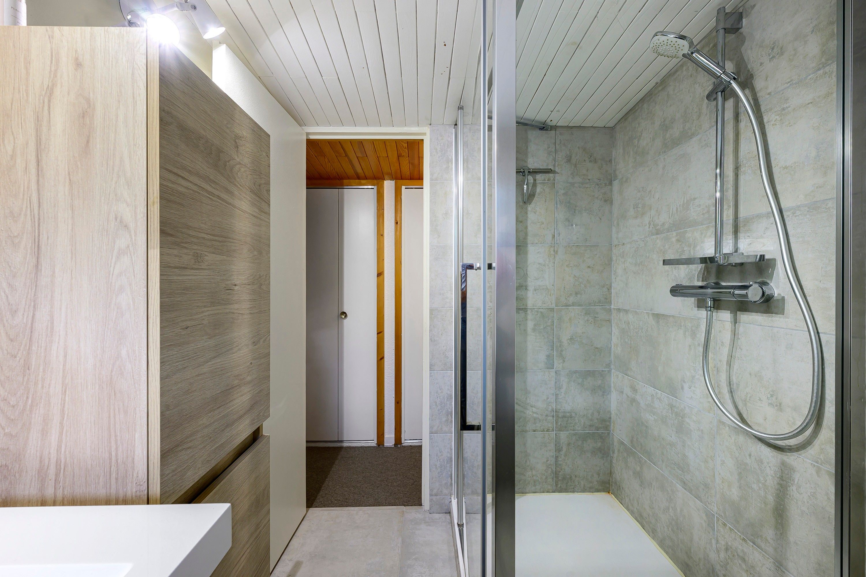 A modern bathroom with a glass shower enclosure, a wooden vanity, and a tiled shower wall.