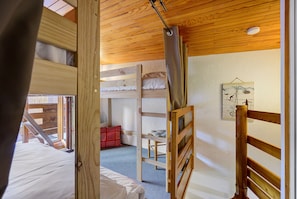 A room with bunk beds, a ladder, a wooden ceiling, and a wall-mounted picture.