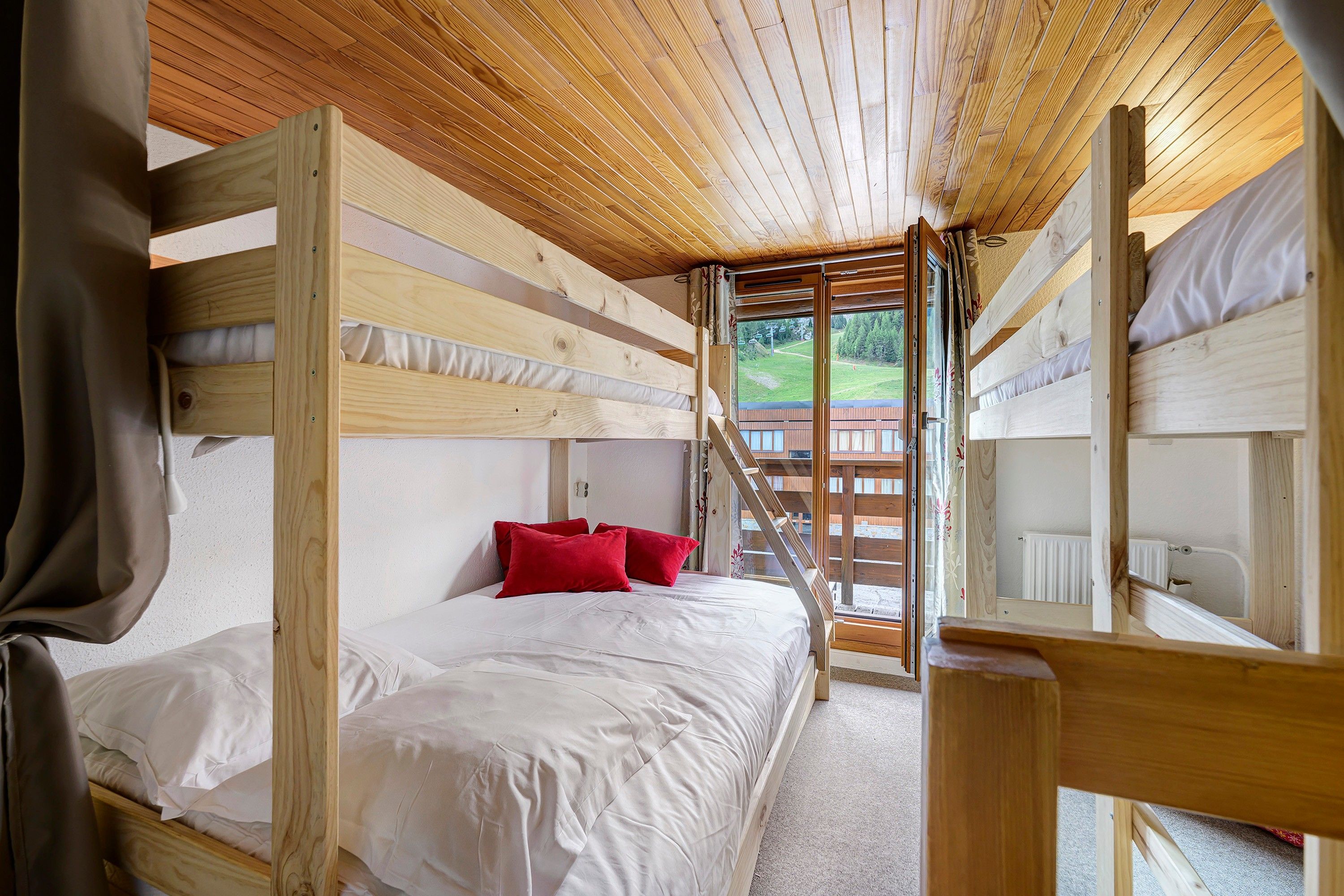 Une chambre avec des lits superposés, un plafond en bois et une fenêtre donnant sur un jardin.
