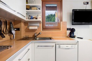 Cocina compacta con lavavajillas integrado, un lavamanos y ventana con vistas a un balcón.