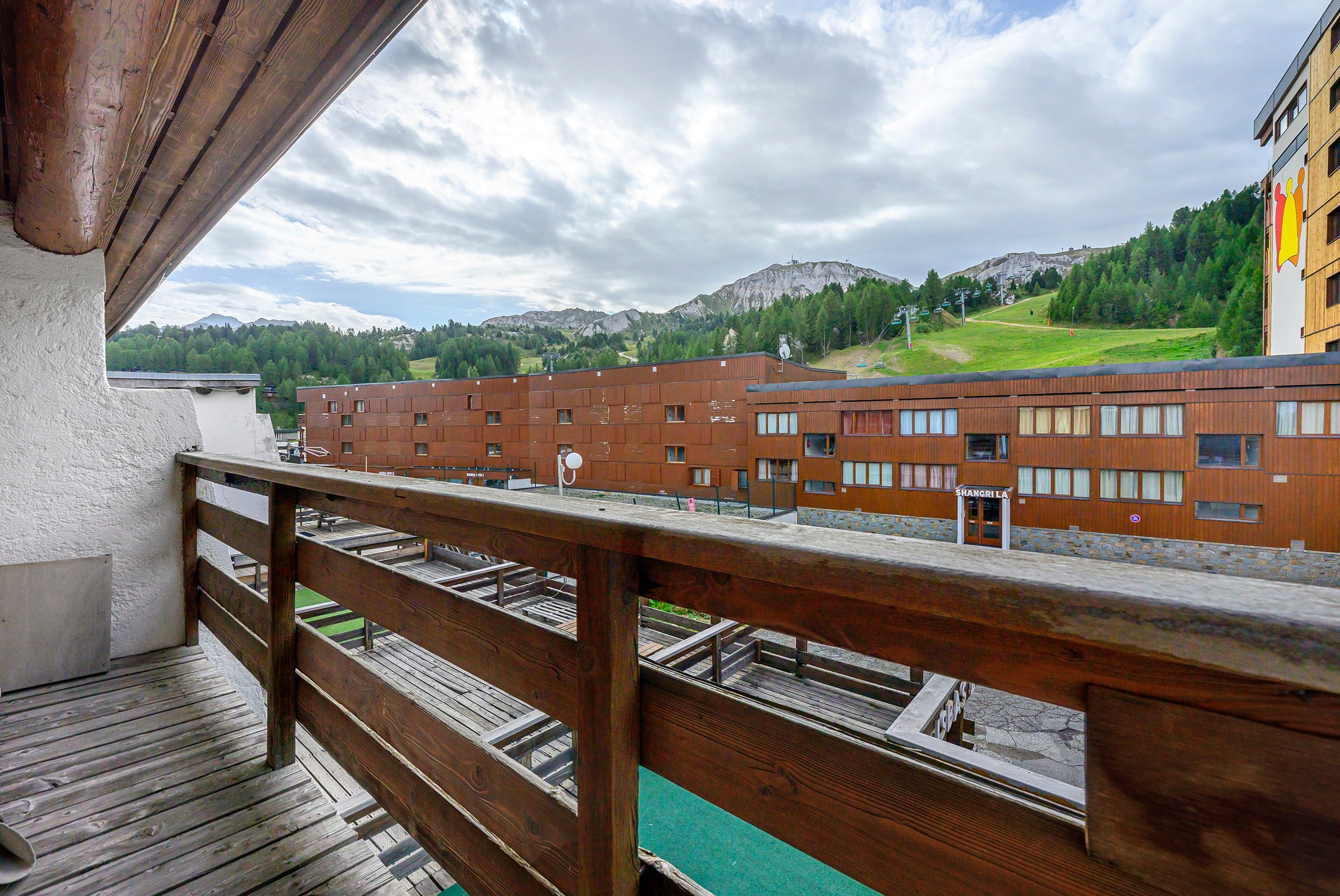 A wooden balcony overlooking a row of brick buildings with a mountain in the background.
