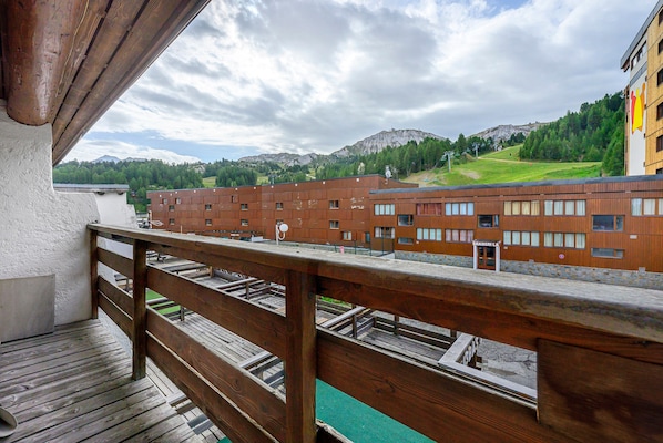 A wooden balcony overlooking a row of brick buildings with a mountain in the background.