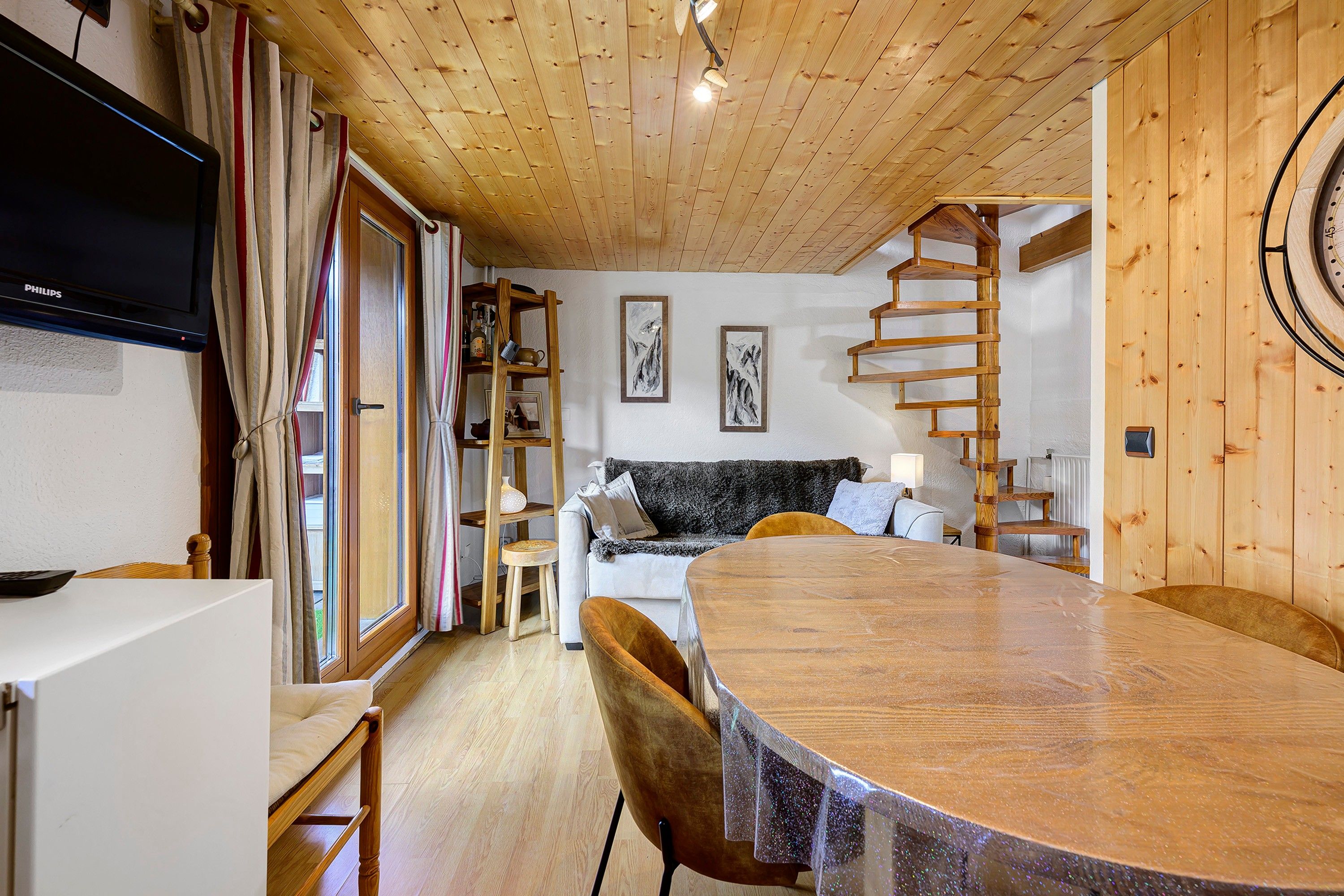 A cozy wooden interior with a dining table, a sofa, and a staircase.