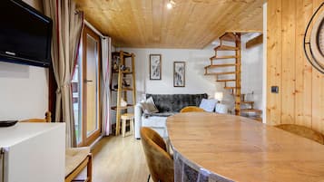 A cozy wooden interior with a dining table, a sofa, and a staircase.