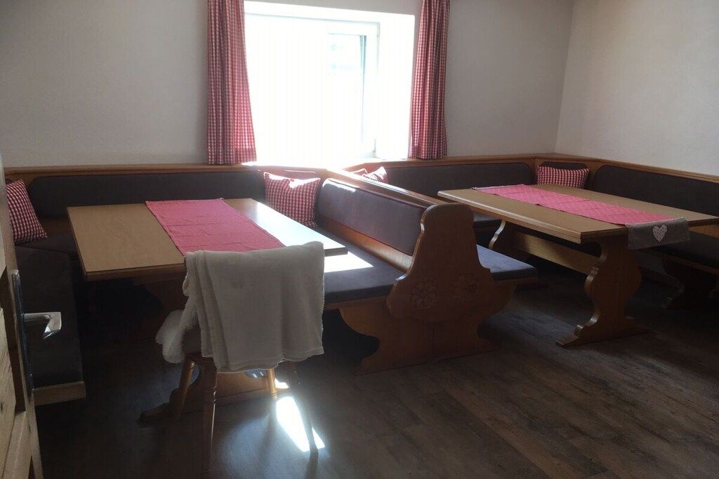 A room with a wooden floor, a bench, a table, and a window with curtains.