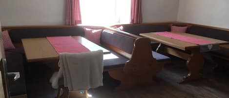 A room with a wooden floor, a bench, a table, and a window with curtains.