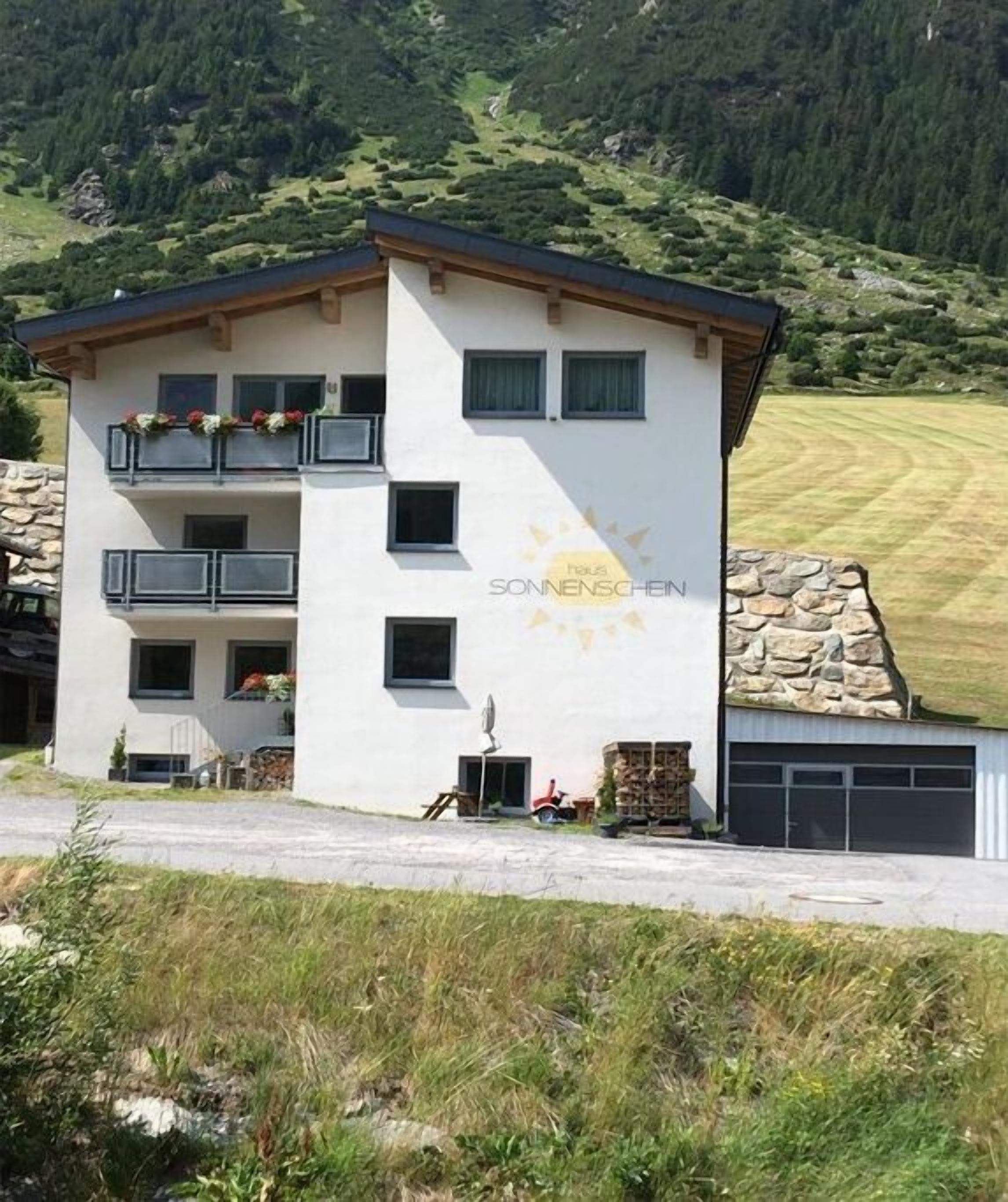 Un immeuble de deux étages avec une façade en pierre, des balcons ornés de jardinières et un garage.