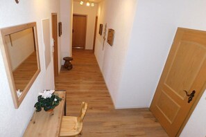 Ein Korridor mit Holzboden, einer Holztür, einer Bank mit Pflanze und einem Spiegel an der Wand.