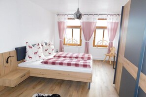 Ein Schlafzimmer mit einem Bett, einem Sessel, einem Fenster mit Vorhängen und einer Pendelleuchte.