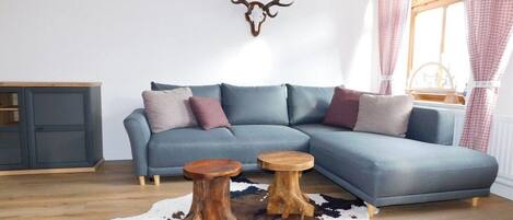 A modern living room with a sectional sofa, two wooden stools, a cowhide rug, and a mounted deer head on the wall.