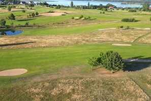 Ein Golfplatz mit Bunkern, einem Teich und einem Wasserspiegel im Hintergrund.