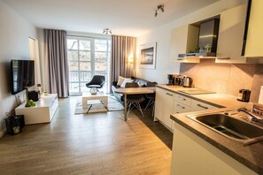 Ein modernes Wohnzimmer mit einer Couch, einem Couchtisch und einem Fernseher. Es gibt einen Essbereich mit Stühlen und einem Tisch. Die Küche verfügt über ein Spülbecken und Schränke.
