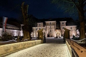 Ein historisches Gebäude mit einem Kopfsteinpflasterhof, großen Bäumen und einer Flagge.