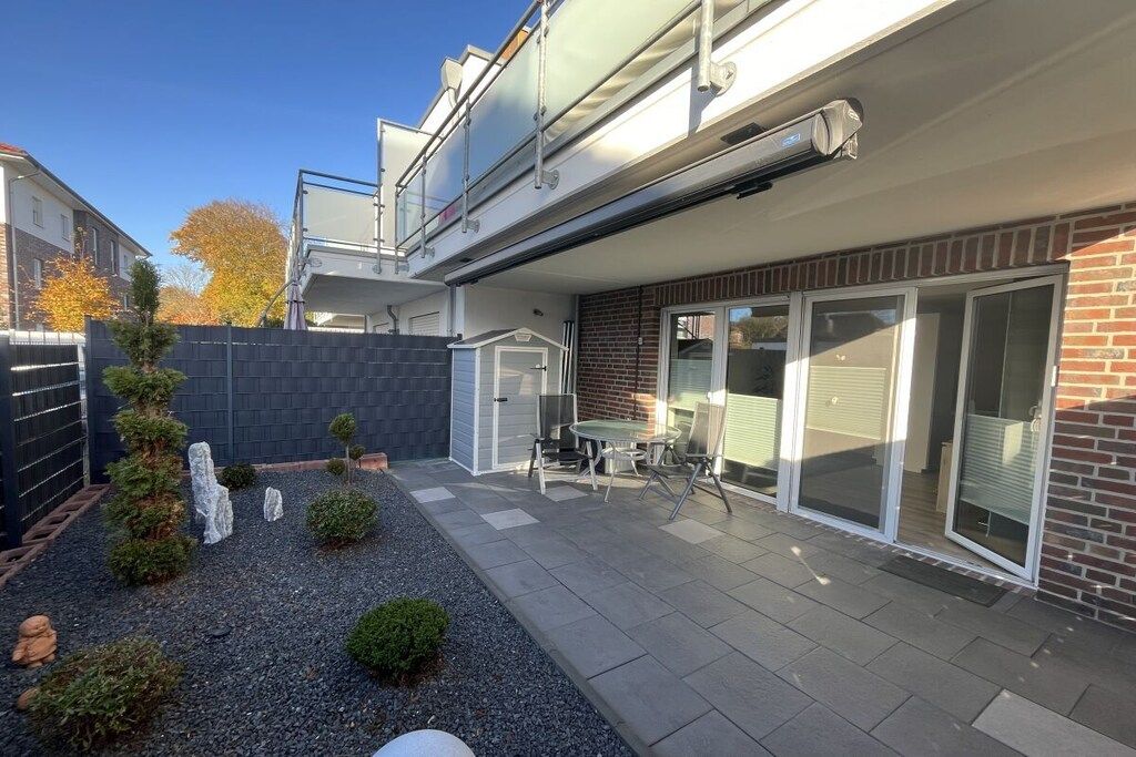 Ein modernes Wohngebäude mit einer Terrassenfläche, ausgestattet mit Tisch und Stühlen, einem kleinen Garten mit Steinen und Pflanzen sowie einer Ziegel-Fassade.