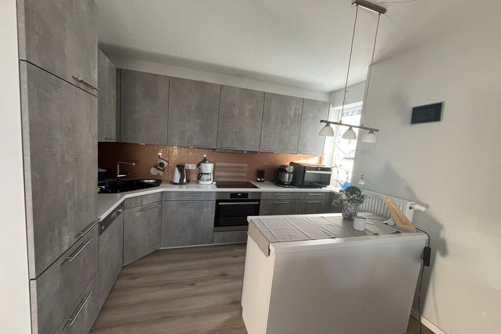 Une cuisine moderne avec des meubles gris, un four encastré et un réfrigérateur blanc.