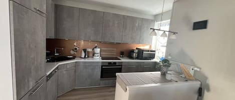 Una cocina moderna con armarios grises, horno empotrado y refrigerador blanco.