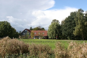 A house with a red roof, surrounded by a grassy field and trees. - Holiday apartment with 3 bedrooms (Wangerland)