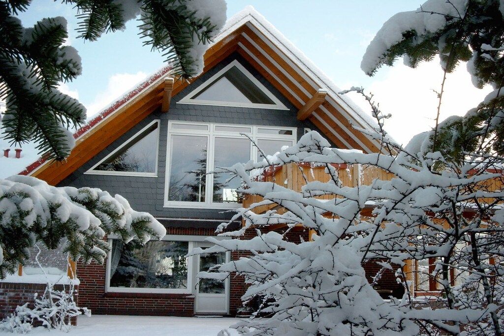 A two-story house with a sloped roof, large windows, and a brick foundation.
